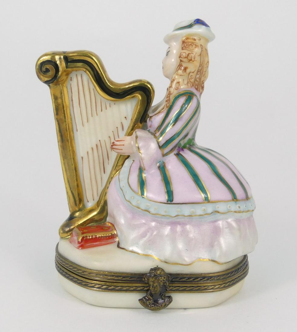 LIMOGES 'HARP PLAYER' PORCELAIN TRINKET BOX: Limoges porcelain trinket box in the form of a lady playing harp. Marked to underside. Measures 3 1/4" height.