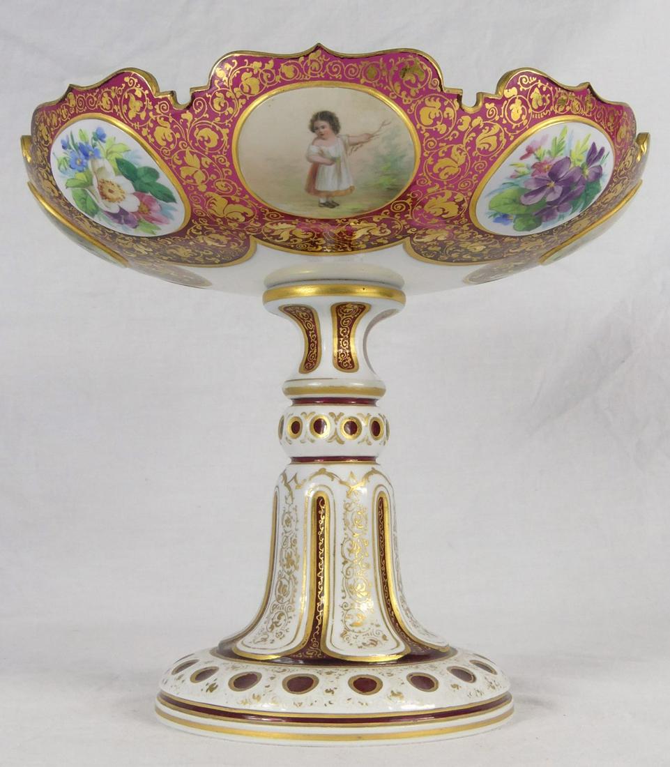 BOHEMIAN WHITE CUT TO CRANBERRY COMPOTE: Bohemian cranberry glass compote with white cut-back overlay. Decorated with hand painted panels of children and florals. Measures 8" height x 8 7/8" diameter.