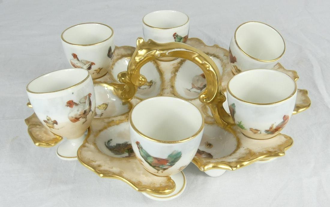 7pc LIMOGES PORCELAIN EGG SET: Limoges porcelain egg set includes six porcelain egg cups and handled tray. Each piece decorated with hen and chick motif with gilt accents. Tray marked to underside. Tray measures 9" length. Cups mea