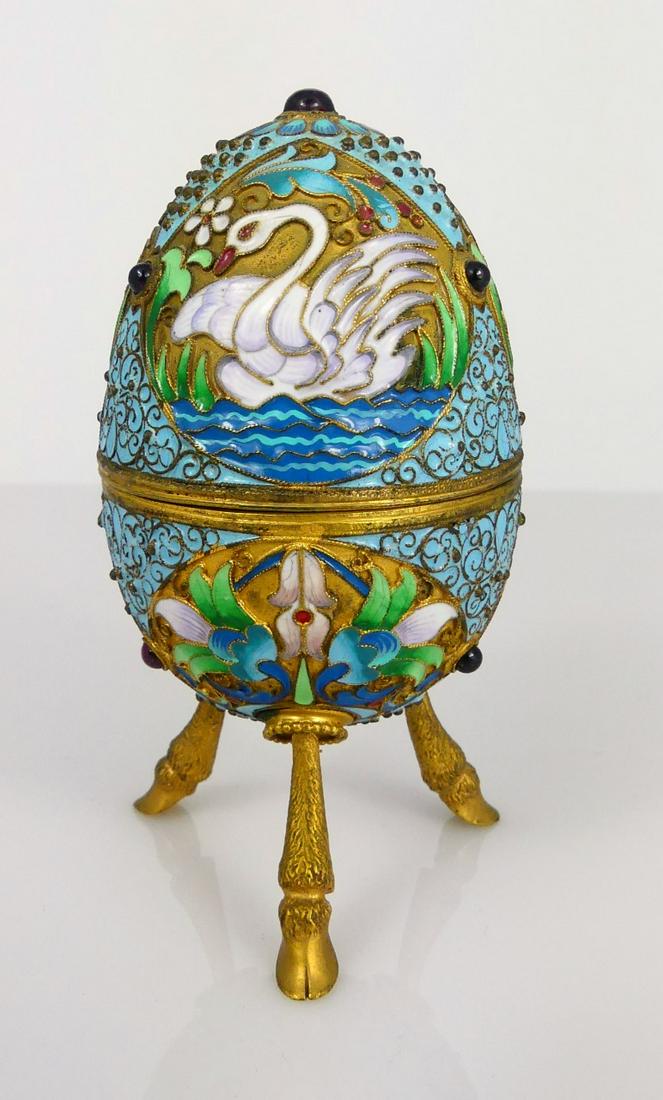 RUSSIAN SILVER ENAMELED EGG BOX: Russian silver, enamel and ruby box in the form of an egg with tripod goat hoof feet. Decorated with swans and flowers. Marked 84 with additional markings to interior of each piece. Measures 3 3/4" ov