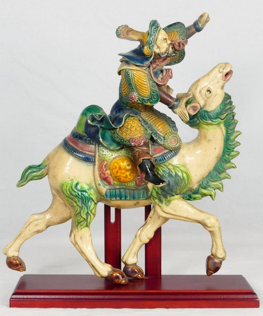 CHINESE POLYCHROME ROOF TILE RIDER ON CAMEL: Chinese polychrome figural roof tile depicting a warrior riding a camel. Measures 12 1/2" length x 14 3/4" height + 1" wooden base.