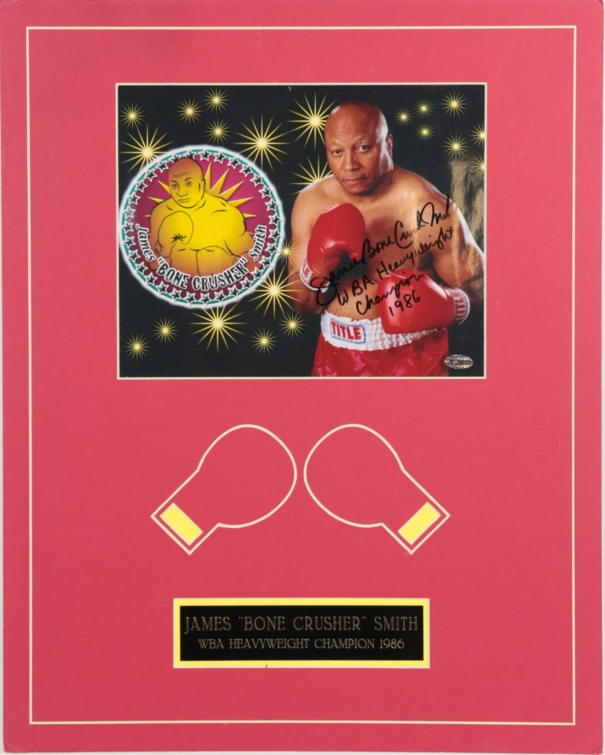 JAMES 'BONE CRUSHER' SMITH SIGNED PHOTOGRAPH: James Bonecrusher Smith WBA Heavyweight Boxing Champion autographed photo. Includes COA #20H00229. Photo measures 9 3/4" x 7 3/4. Mat measures 20" x 16".