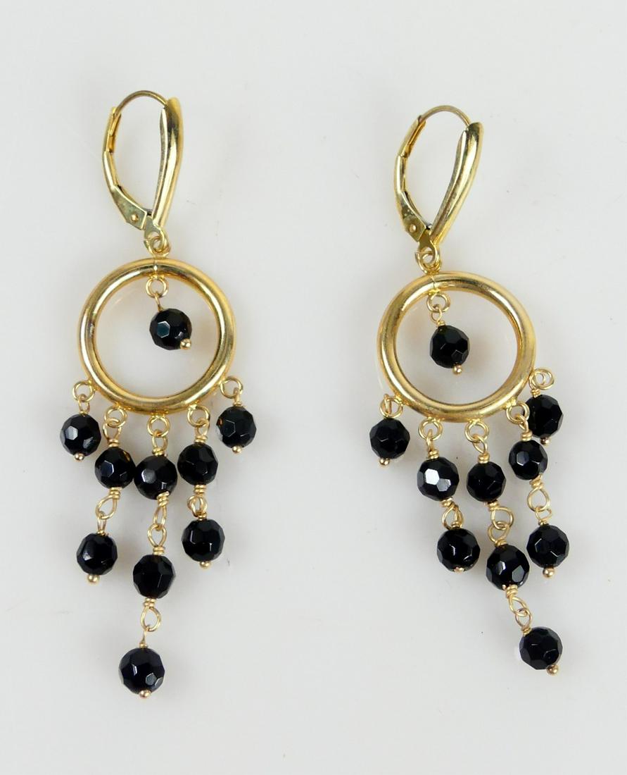 14K YELLOW GOLD ONYX DANGLE HOOP EARRINGS: 14kt yellow gold hoop earrings with faceted onyx beads dangle. Each marked 14K and hallmarked DZ. Each measures 60mm total drop. Total weight 3.9g.