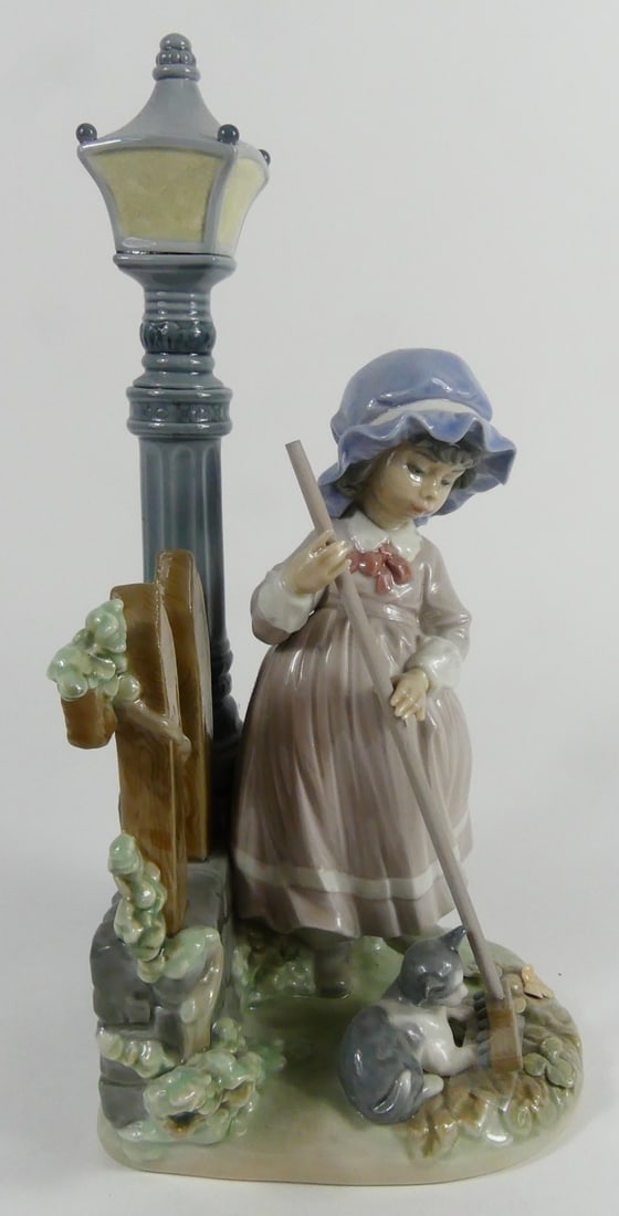 LLADRO 'FALL CLEAN UP' PORCELAIN FIGURINE: Lladro porcelain figure titled 'Fall Clean Up' #5286. Depicts a girl raking leaves beside her cat with a lantern in the background. Marked to underside. Measures 12 1/2" height.