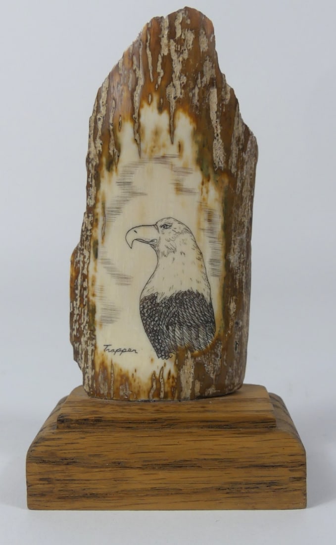 SCRIMSHAW WITH EAGLE SIGNED TRAPPER: Mammoth bark scrimshaw depicting an eagle. Signed Trapper. Measures 3 1/2" + 3/4" wooden base. keyword: inuit
