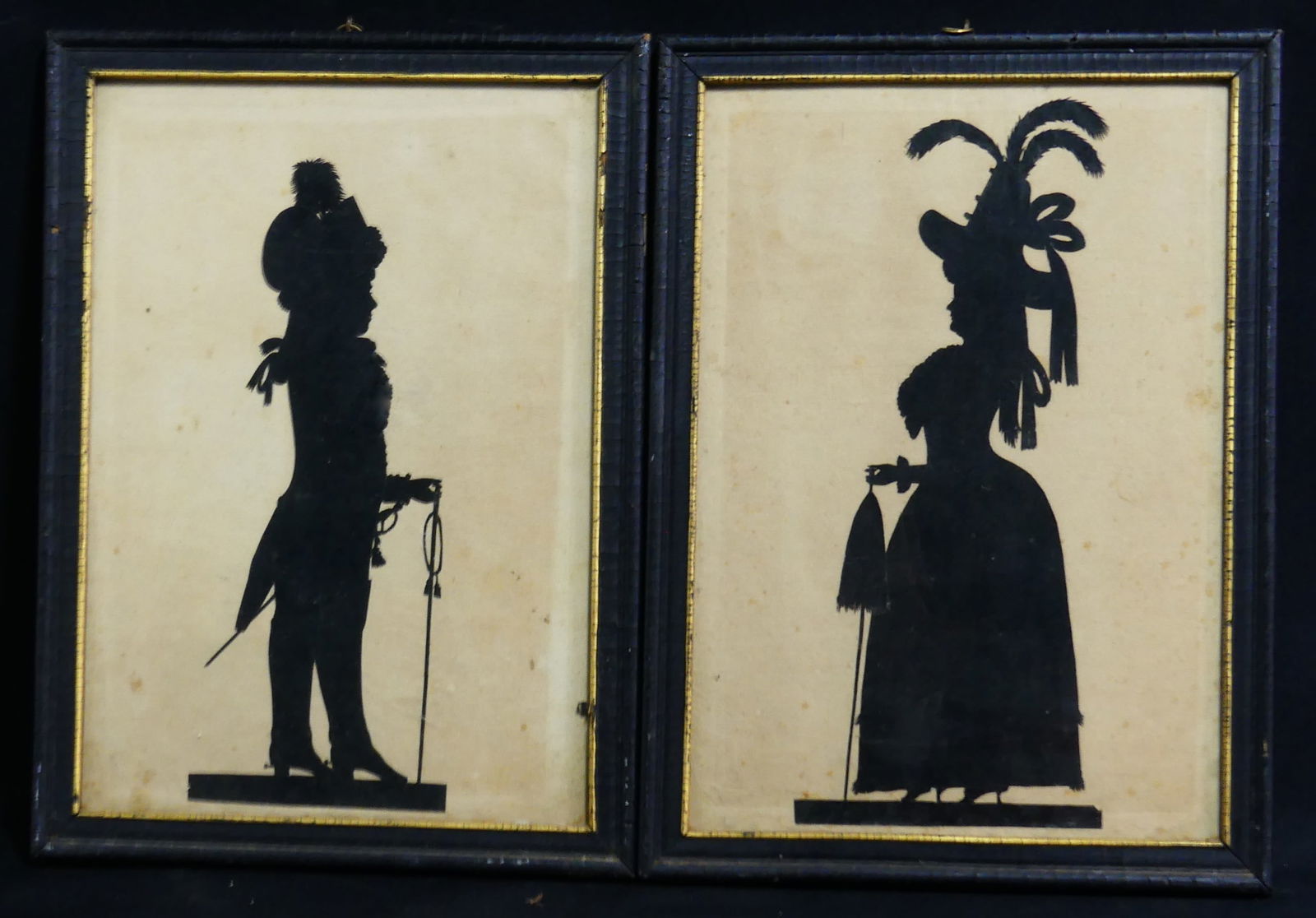 PR SILHOUETTE CUT OUTS: Two silhouette cut outs including a soldier with sword and walking stick and well-dressed woman with umbrella. Each frame measures 12 3/8" x 9 1/8".