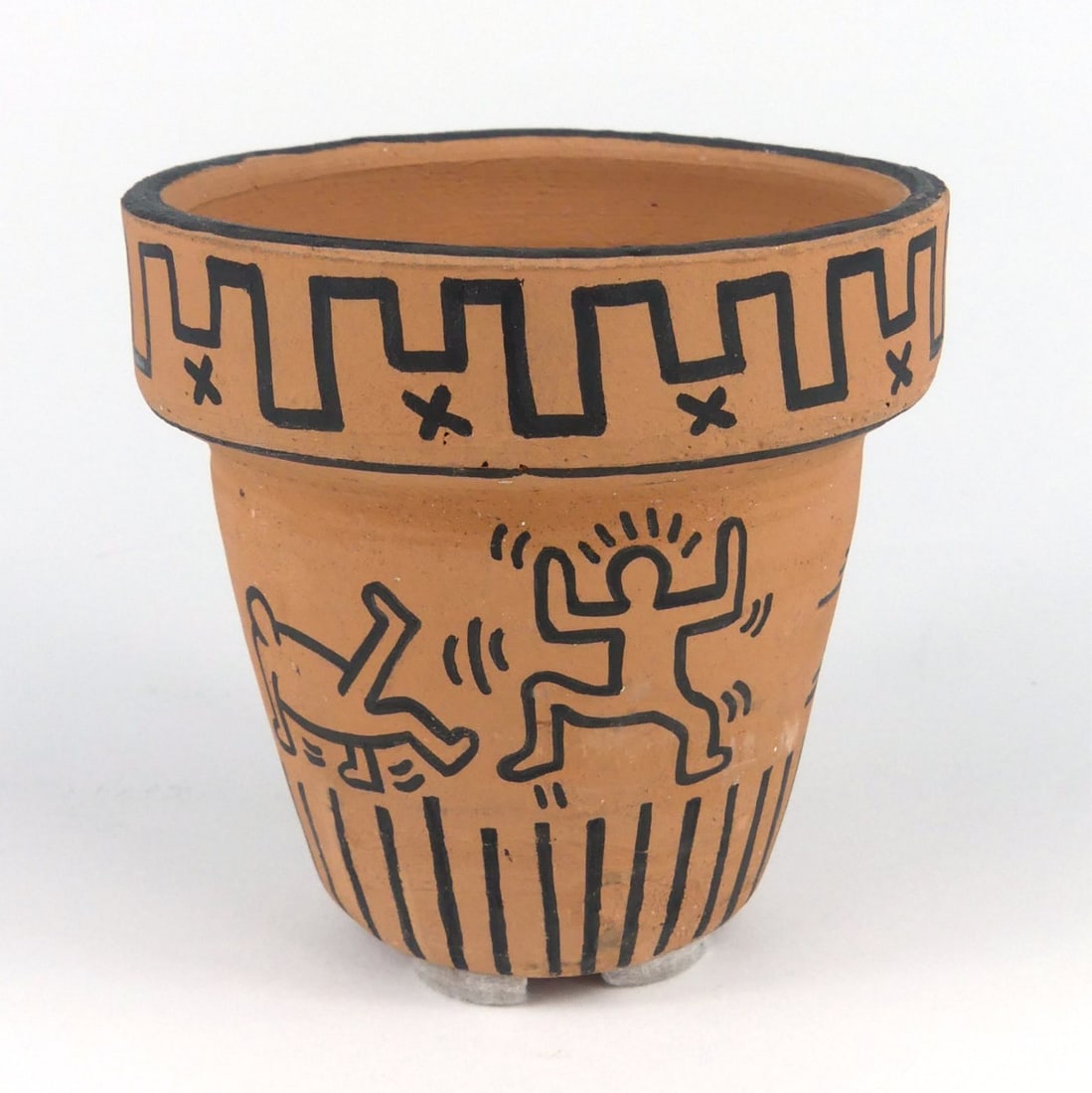 KEITH HARING TERRA COTTA POT: Keith Haring [attributed] black marker on terracotta flower pot. Depicts dancing figures with geometric designs. Signed and dated 1982 to underside. Measures 3 3/4" x 3 3/4" x 3 5/8".