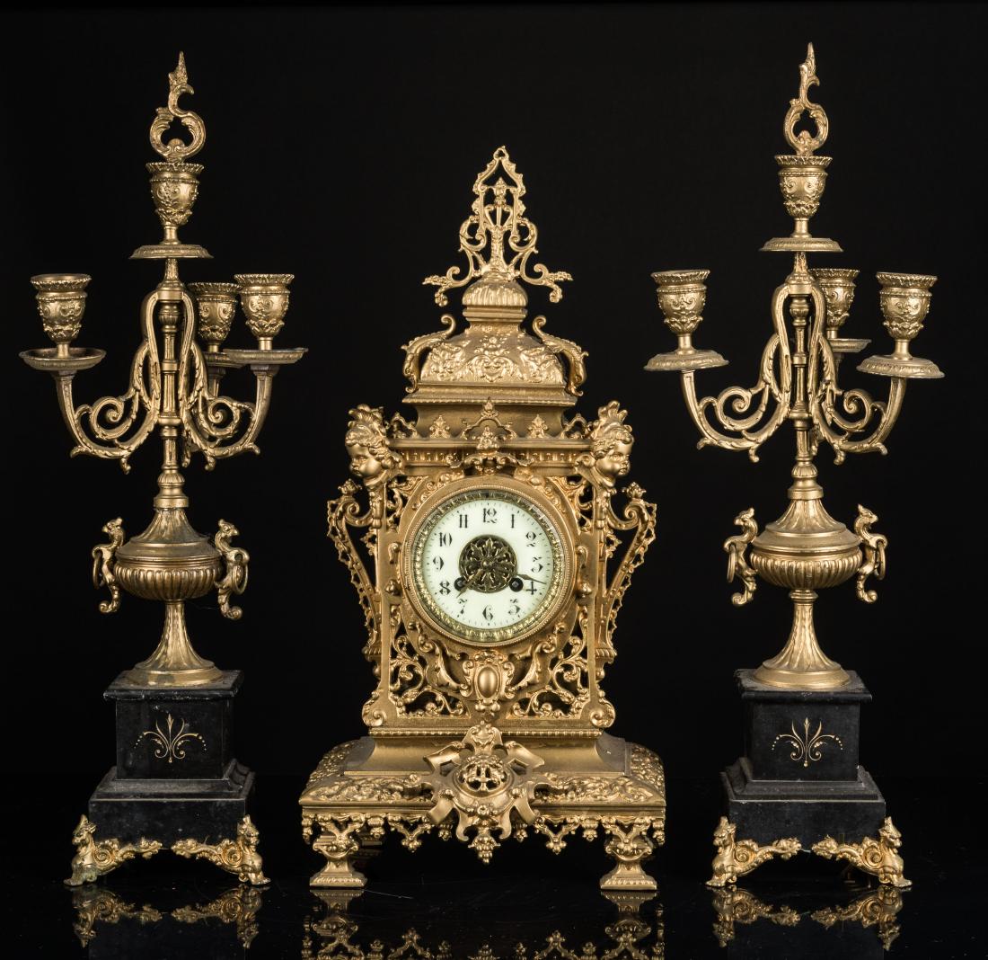 Vintage / Antique Clock & Candelabra Mantle Garniture: A large and imposing gilt mantle garniture comprising an ornate chiming clock with black on white enameled Arabic numerals with matching pair of sextuple candlesticks, including caps for central candl