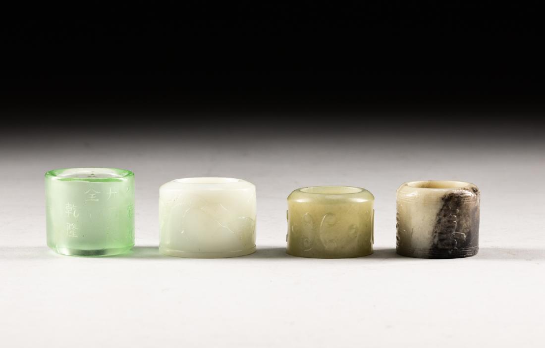 Set Of Four Antique Jade Thumb Rings: Each varying in size, all cylindrical form, one jade thumb ring of the translucent stone of an even white tone, one glass ring, the exterior inscribed with an imperial poem, the glass of pale greenish
