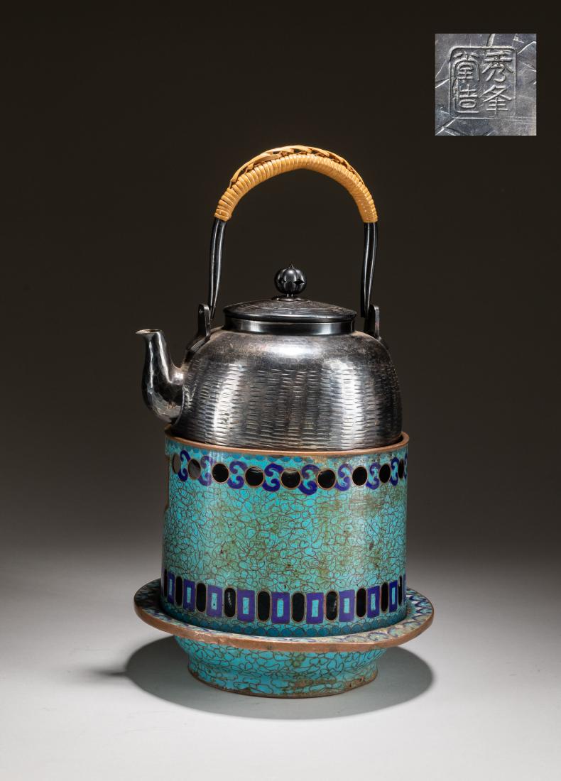 19th Japanese Antique Silver Teapot: The cylindrical body supported by a base with canted shoulders set with a loop handle opposite a cured spout, surmounted by a tall handle, all display on the cloisonne enamel base with metal liner. 6.