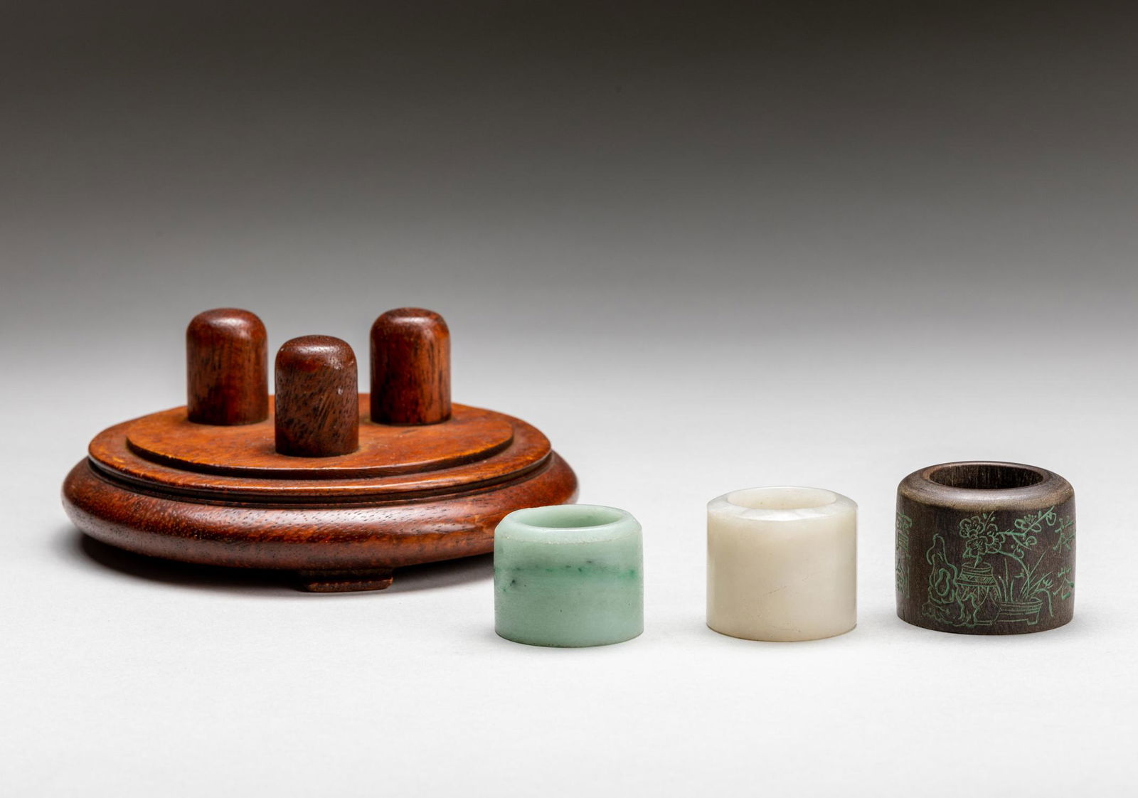 Set Of Chinese Antique Jade Thumb Rings: Set of three pieces, each of short cylindrical form, one jadeite thumb ring, one white jade thumb and one agarwood thumb rings, the exterior inscribed with a poem, all display on a fitted wood stand.