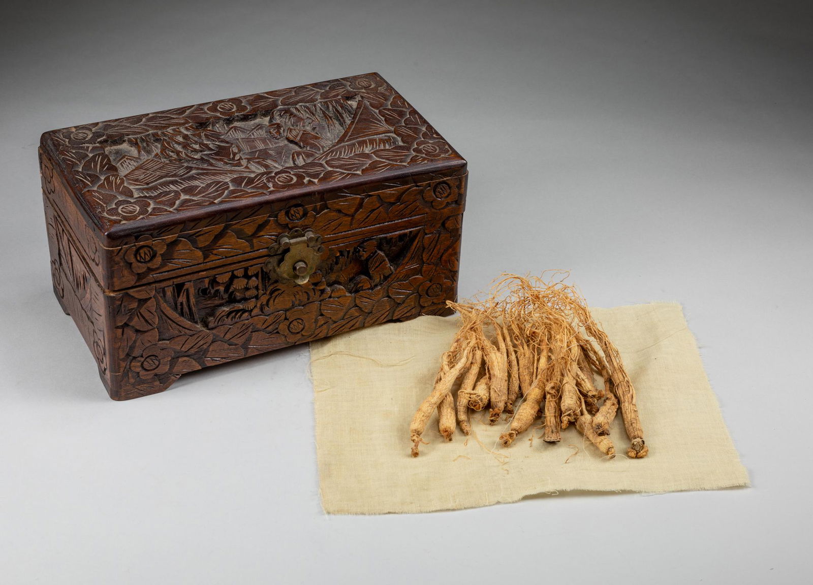 Group 1900s Korean Antique Ginsengs.: The camphor wood box contains seventeen pieces of ginsengs, the box of massive rectangular form, supported on a tall shaped base, each side carved in low relief an elder man in sitting position, surro