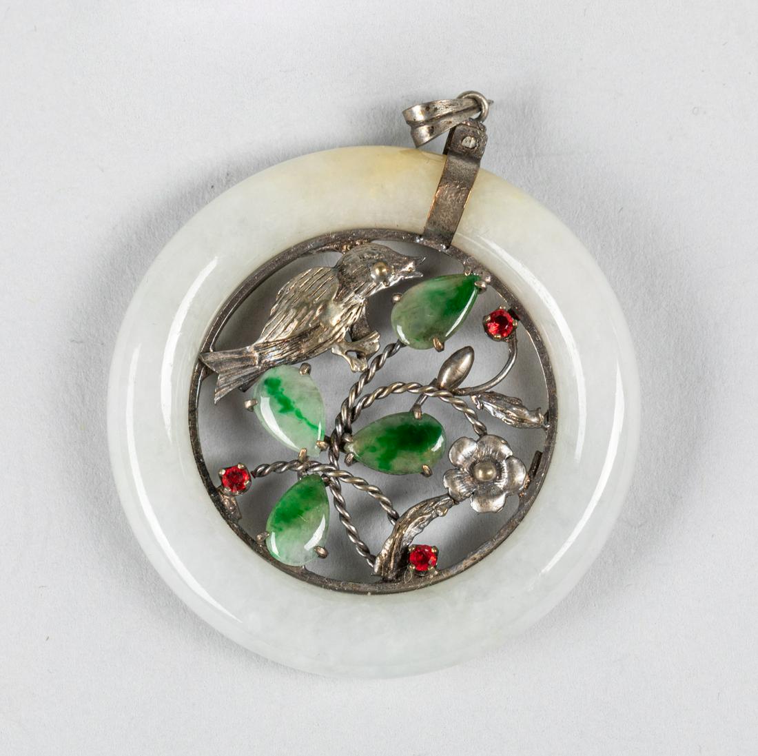 Chinese Jade Sterling Silver Pendant: Of circular form, the central decorated with a bird resting on a leafy stems, highlight with apple green jadeite leafy, and red gemstones. 1.75 inch diameter