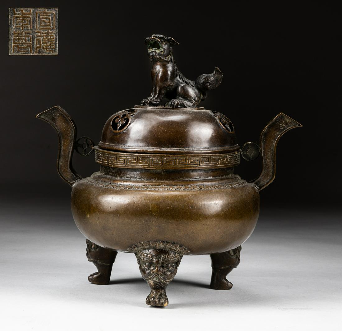 Japanese Meiji Bronze Tripod Incense Burner: The shallow body encircled with a raised fillet and supported on three legs, flanked by a pair of upright loop handles, the openwork cover with a lion-dog finial, the base inscribed with four characte