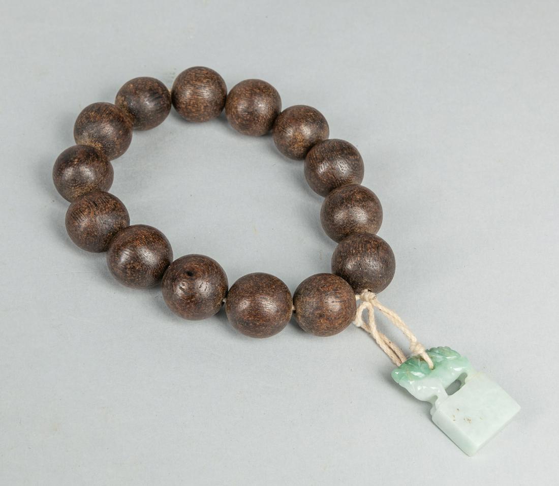 Large Bead Chinese Agarwood Prayer Beads with Jadeite: Large 14 beads Chinese agarwood prayer beads with jadeite seal carved mythical beast on the top. 1.18 inch L (largest beads). The Estate of the Yaotome, Long Beach, CA, 2000.