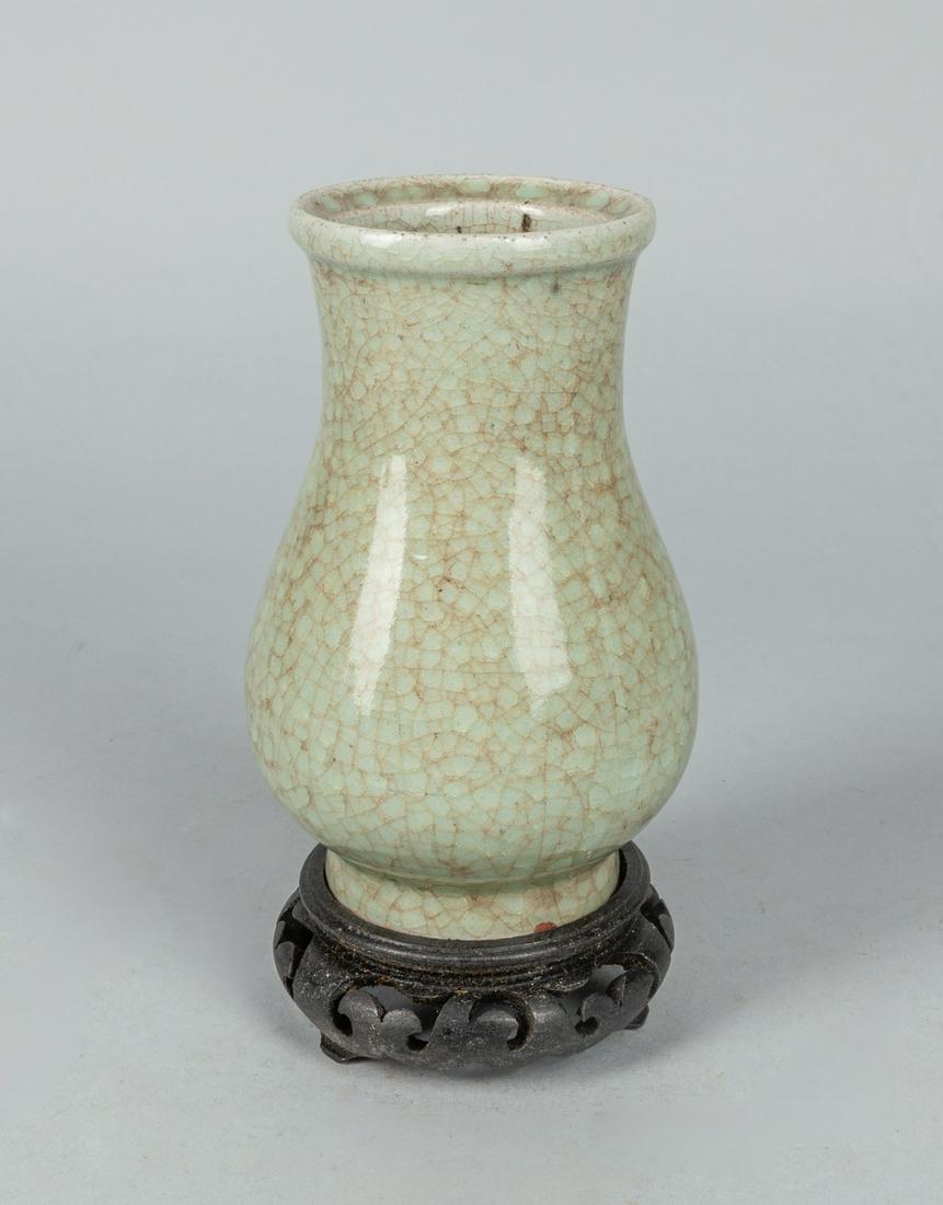 Chinese Crack Glazed Porcelain Vase: The pear shaped body rising from a short spreading foot to a trumpet neck set, crack line type glazed in tone of pale celadon with wood stand. 3.7*6.6 inch. The Estate of the See Huan, 1998.