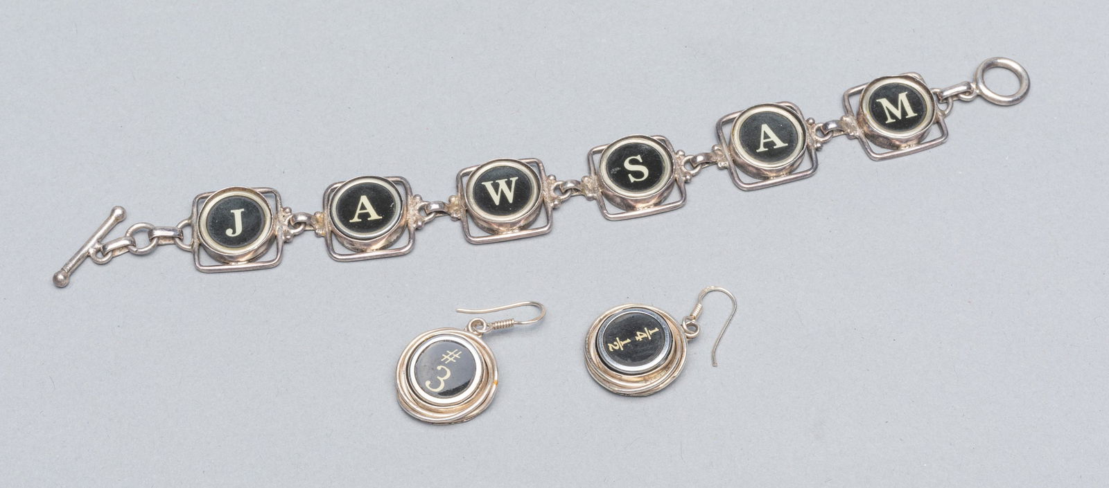 Designed Sterling Typewriter Key Type Bracelet &: Group of three sterling typewriter key type bracelet & Earrings: one bracelet marked 825; two number and symbol earning. 49g W.