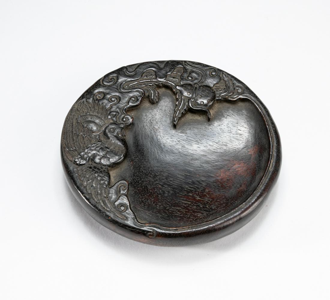 Chinese Zitan Like Wood Inkstone: Of circular section with a continuous foot around the side, the sloping well carved at one end with a phoenix, detailed with cloud scroll and double gourd, the base carved with a four-clawed dragon in