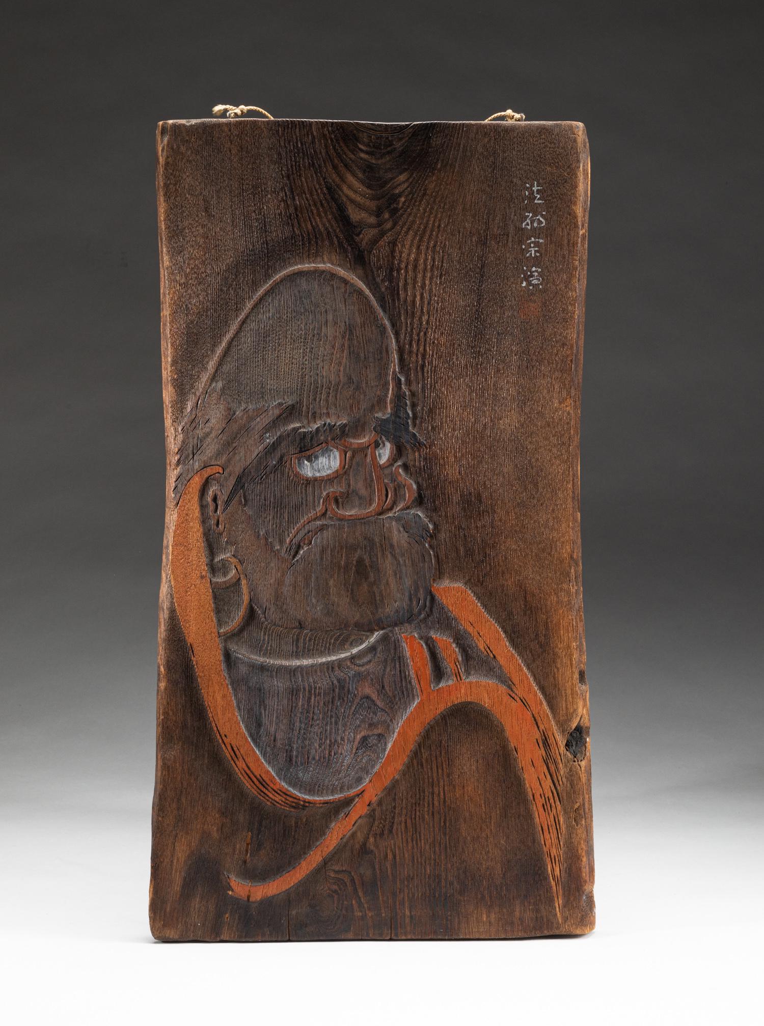 Japanese Meiji Wood Carving Hanging Plaque: Japanese Meiji type wood hanging plaque, carved with a monk with bushy eyebrows and wearing earrings. 20*10.5inch. The Estate of the H. Lopez. Hollywood, CA, 2021.