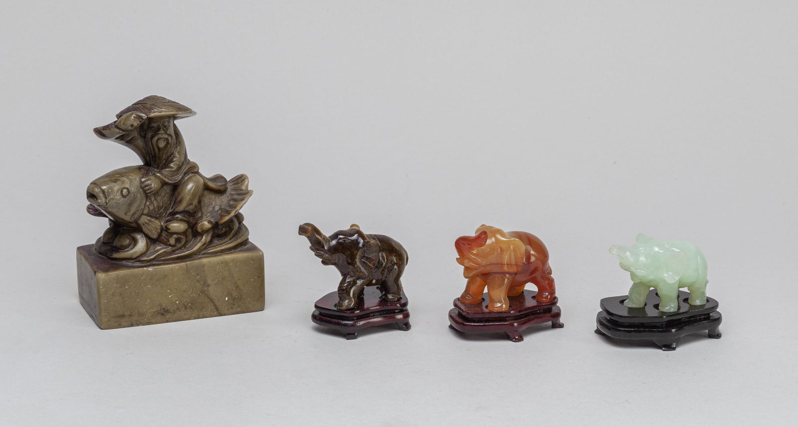 Set Chinese Jade/Stone Sculptures: Including a set of three elephant sculptures in tiger eye stone, agate and jade, each with a wood stand, and a stone sculpture carved as a figure riding on fish. 4.3*3.4*2inch (largest).