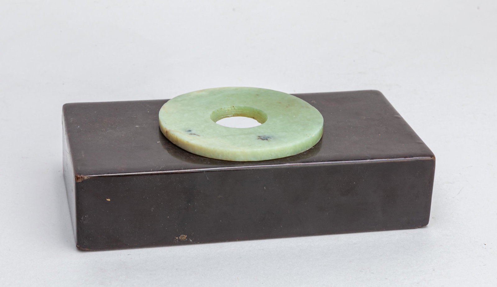 Chinese Jade & Lacquer Stand: Jade disc of circular form, stone of celadon color with black inclusions, with lacquer-wood stand. 5.7inch L, 2.9inch W, 1.5inch H.
