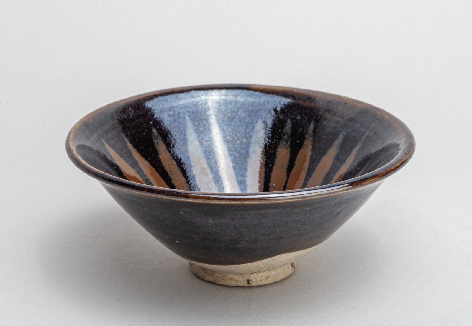 Chinese Jichou Stoneware Porcelain Cup: The interior decorated with a band of upright flower petals reserved in brown glaze against a black ground, the exterior applied with black glaze except the unglazed foot. 1.9inch H, 4.5inch D.