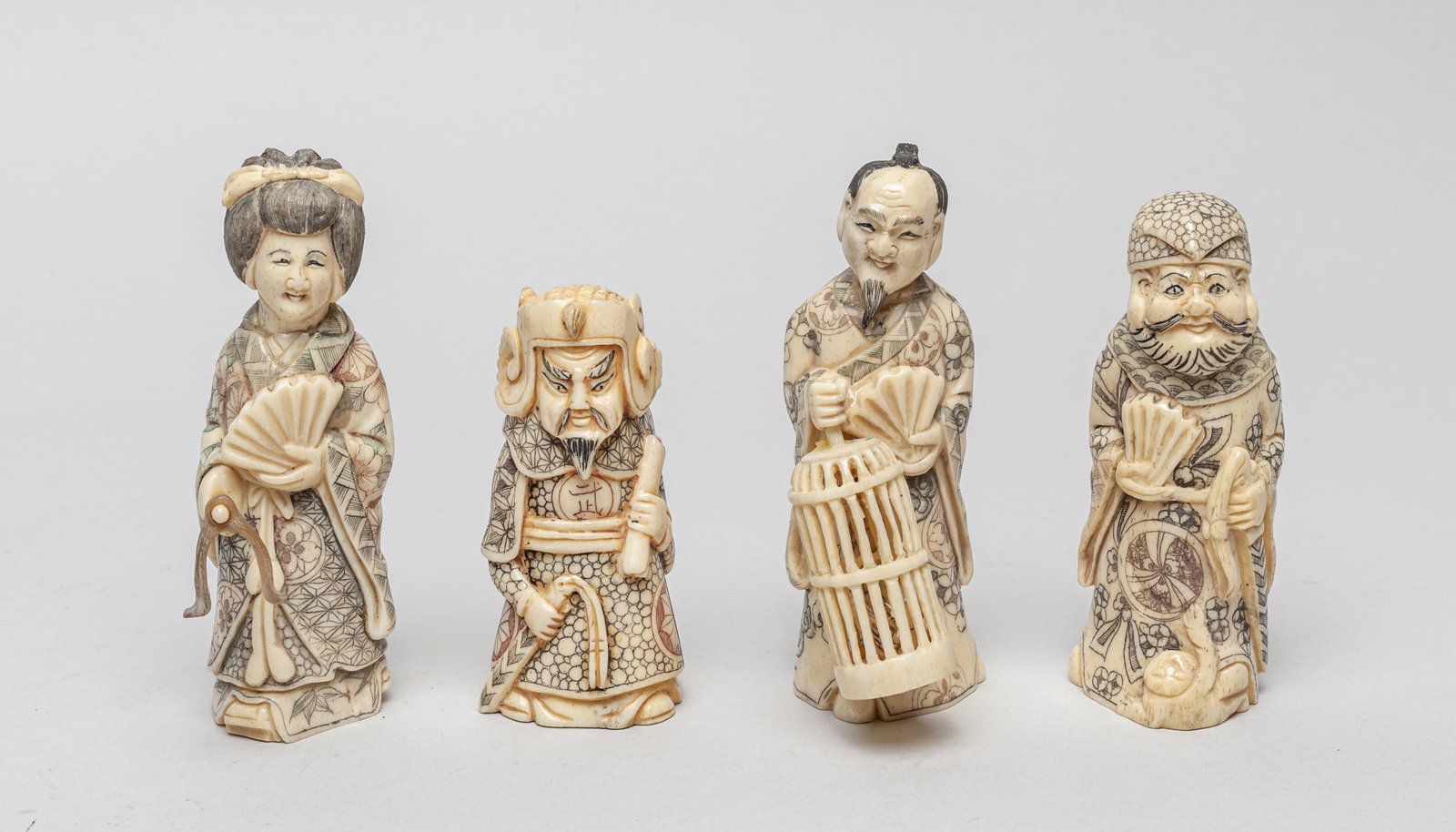 Collectible Japanese Carved Figures: Group of four vintage type bone like carved figurines, the figures wearing robes painted with intricately detailed motifs, hands holding sword, fan or bird basket. 4.35inch H, 1.35inch L, 1.7inch W (l