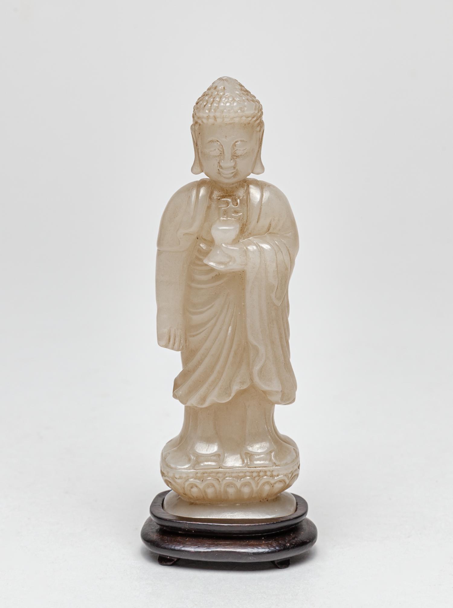Collectible Chinese Jade Carved Buddha: Depicting Buddha standing on a lotus base, wearing a long and flowing robe opening at the chest to reveal a swastika symbol, the left hand holding a bowl, the meditative face surmounted with studded c