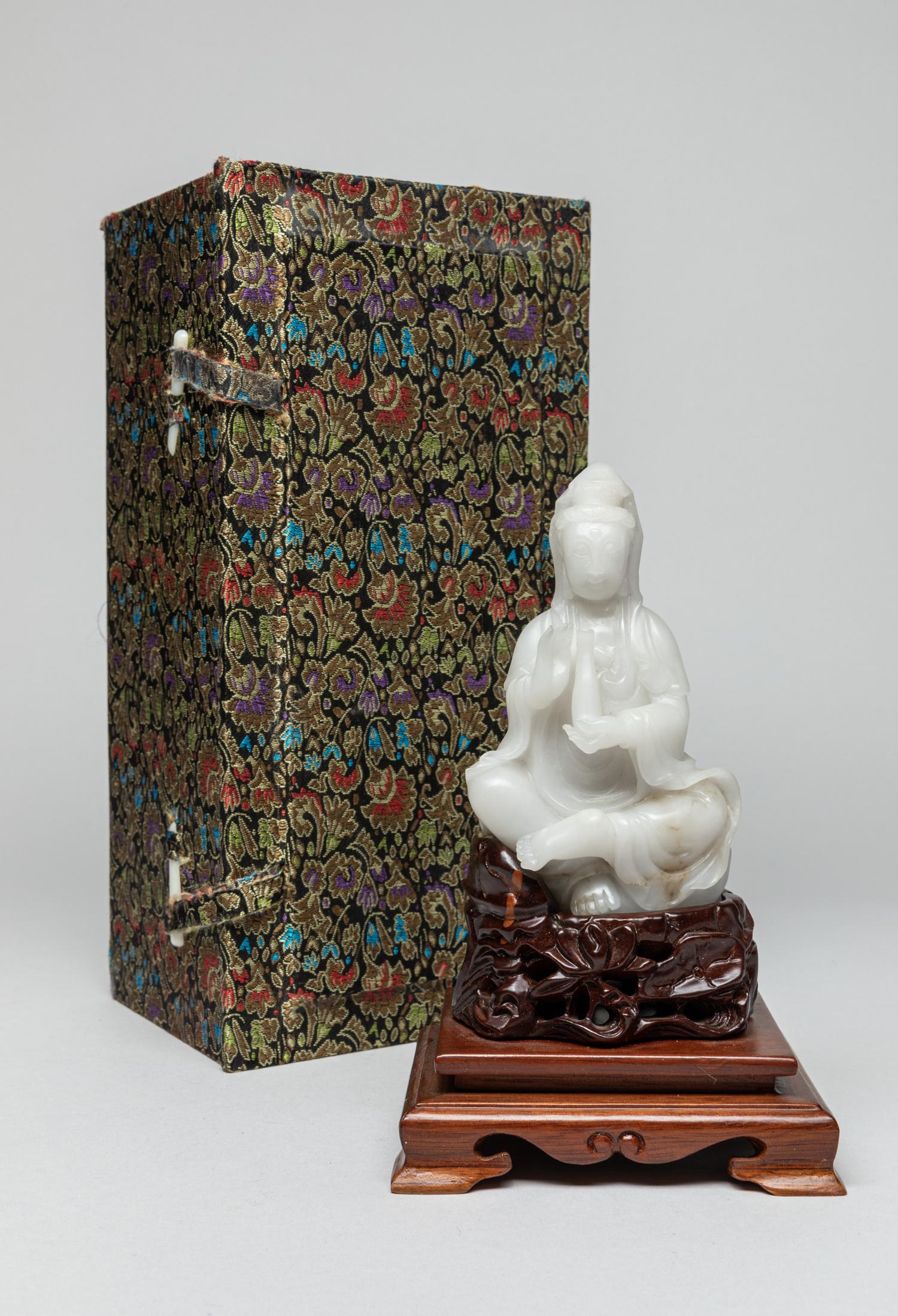 Chinese White Jade Carved Kuanyin: Deftly carved as a seated Kuanyin with left hand holing a bottle and right hand in vitarka mudra, dressed in a long, flowing robe, the semi-translucent white jade with dark inclusions, with a reticula