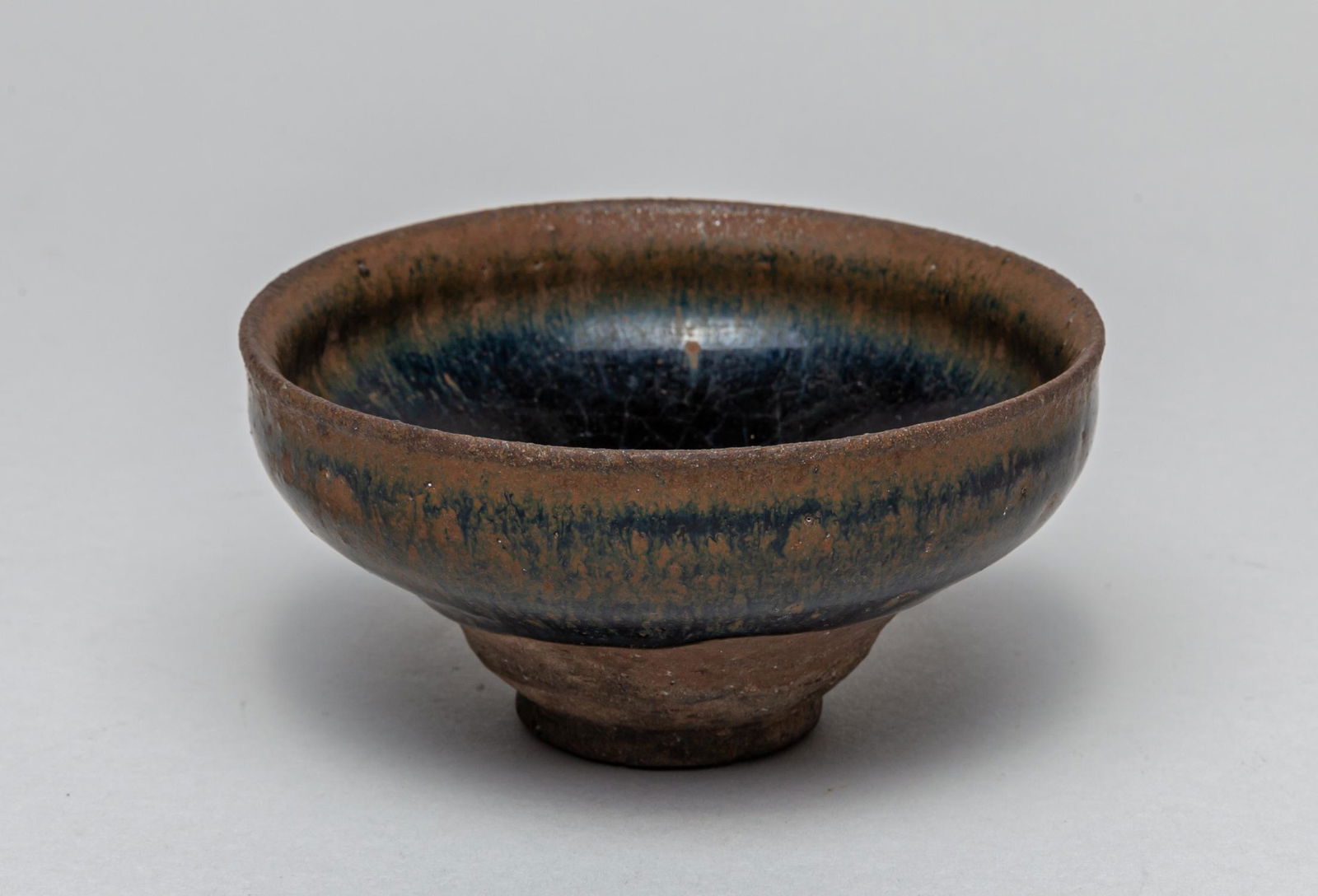 Chinese Jian Stoneware Porcelain Tea Cup: covered overall with a lustrous black glaze suffused with russet streaks extending from the rim down the interior and exterior, the glaze pulling at the rim and stopping short of the foot to reveal th