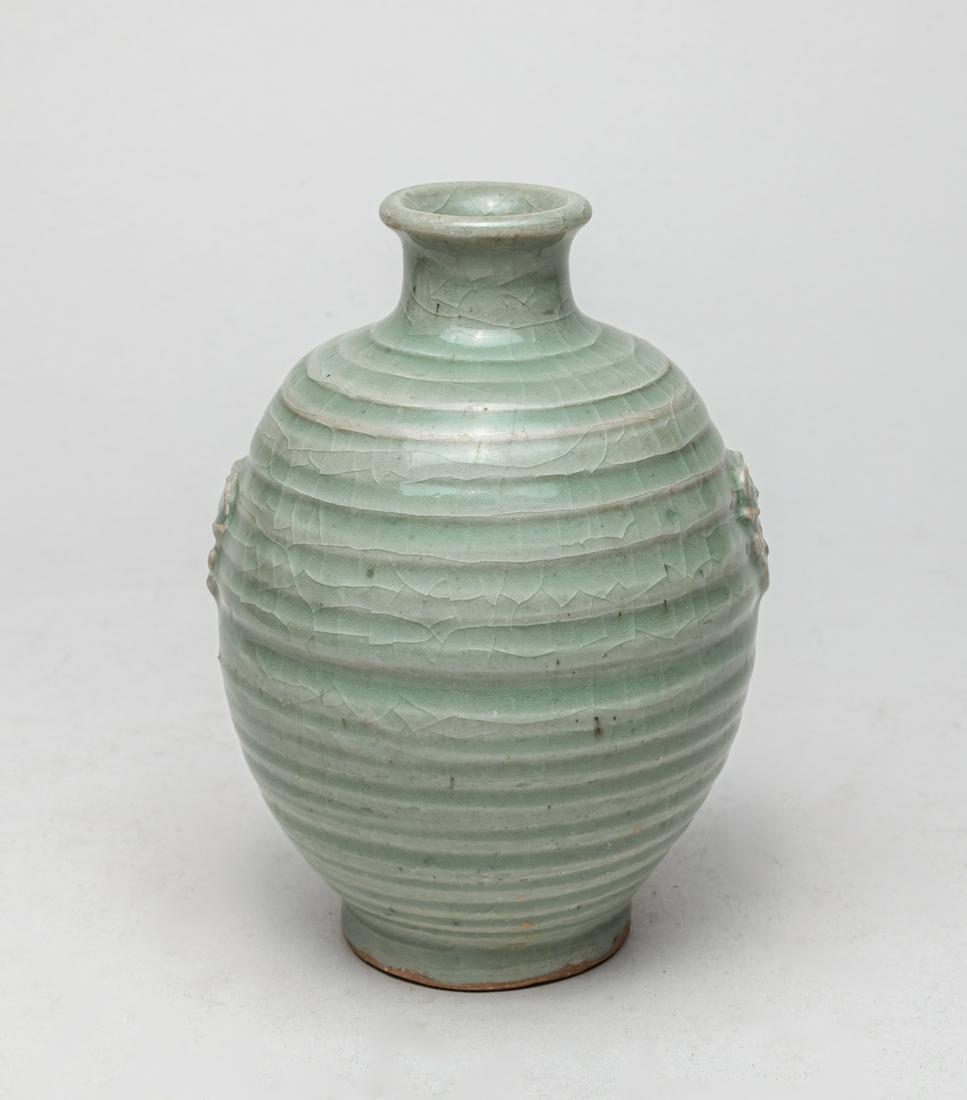 Chinese Yue Type Porcelain Vase: The exterior modeled with repetitive raised bands, flanked with a pair of faux-ring mask handles, the exterior and interior neck covered with a celadon glaze, the unglazed base revealing the brown por