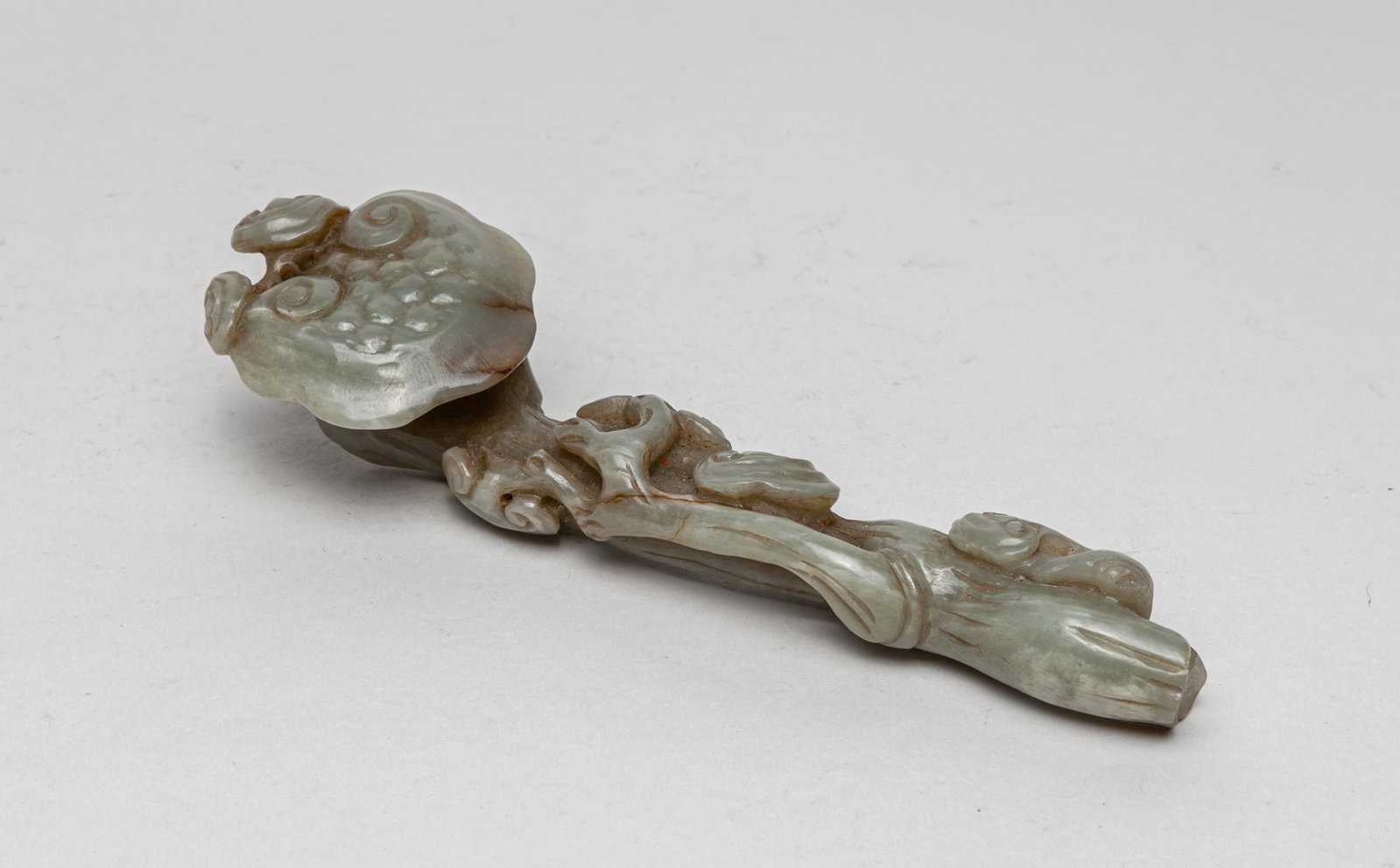 Rare Chinese Jade Carved Ruyi: With the head depicted as four lingzhi blooms, the largest one rendered borne on a gently gnarled branch forming the shaft and issuing more lingzhi blooms, the celadon had eight russet inclusions. 7.5