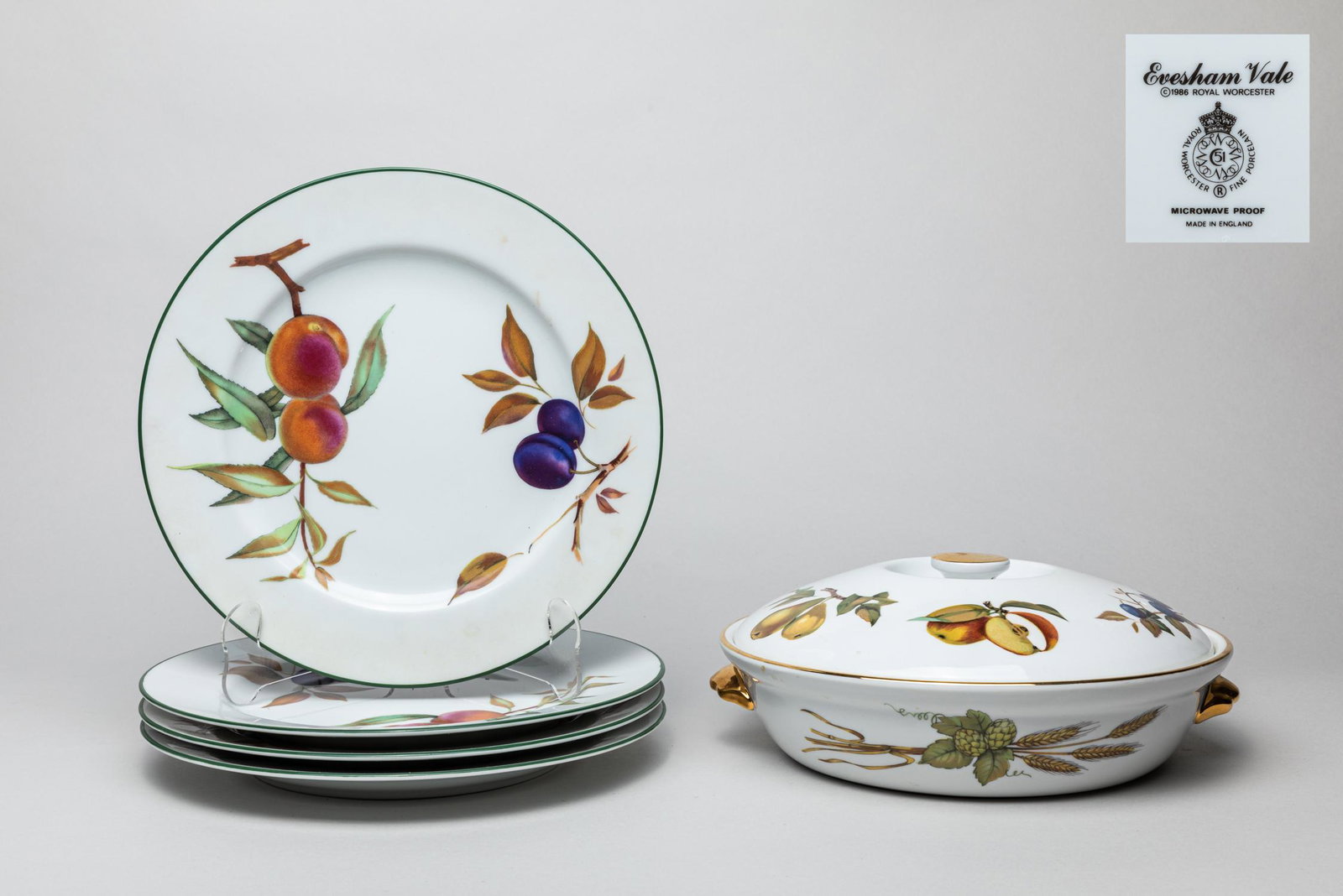 England Evesham Vale Porcelain Flat Wares: Including a covered centerpiece and four plates, delicately painted with various fruits and wheat, each base marked Evesham Vale, Made in England. 10inch D (plate size).
