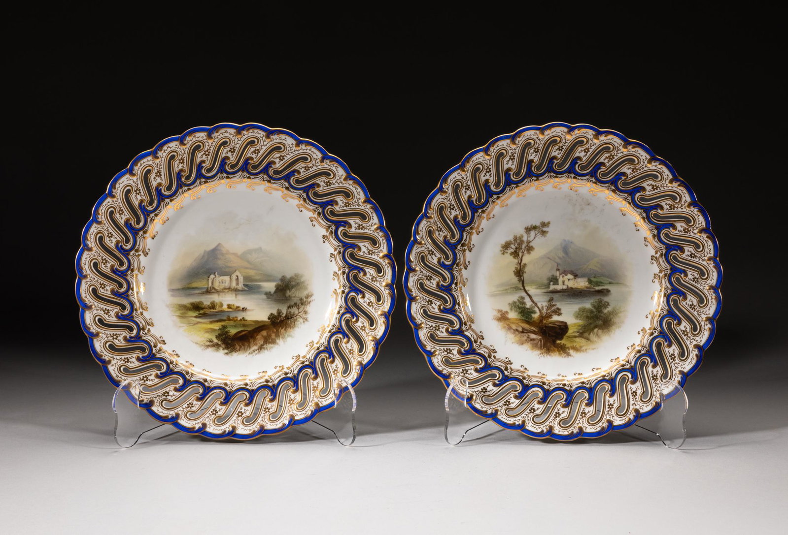 Antique England Davenport Porcelain Plates: A pair of collectible English vintage type porcelain plates, the interior centre painted with river mountainous landscape scene, the openwork rim painted with flower sprays in golden and blue colors. 