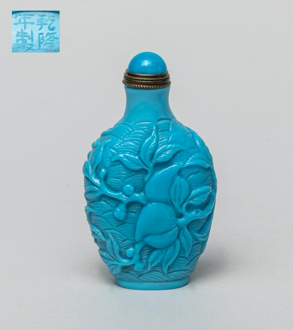 Chinese Carved Peiking Glass Snuff Bottle: Of spade form, the opaque blue glass carved in raised relief with fruiting leafy peach branch against a wave ground, the bottom incised with a four-character mark, with a blue glass stopper. 3.3inch H