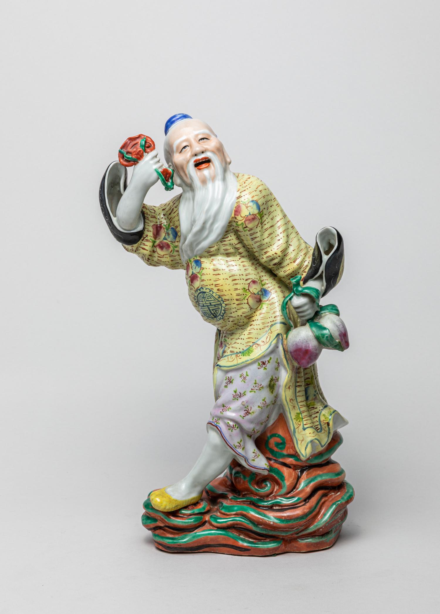 Chinese Famille Rose Porcelain Figure: Modeled as an old figure wearing a long flowing robe painted with peaches and shou characters on a light yellow ground, his left hand holding a peach branch and right hand with lingzhi, standing on sc