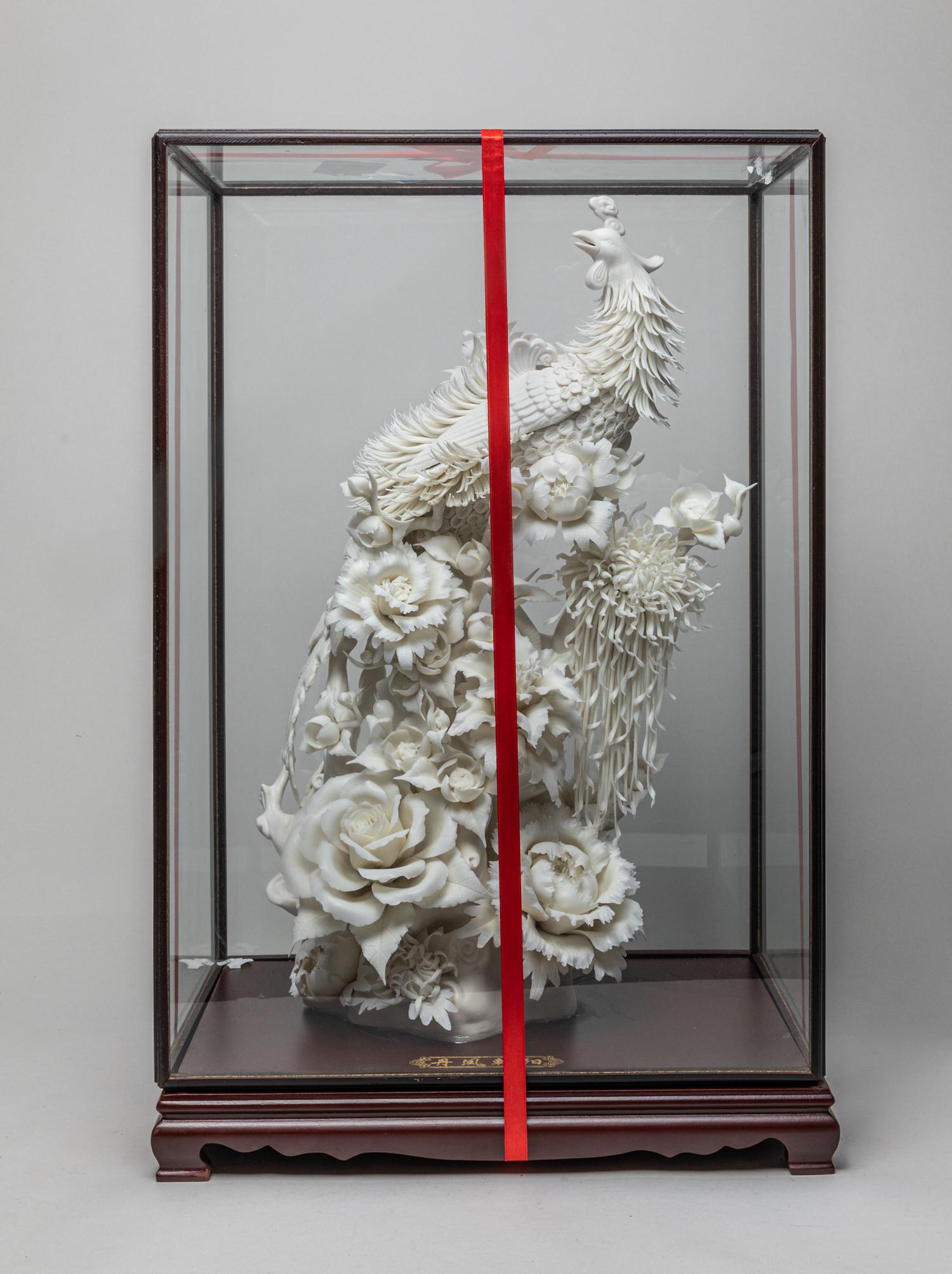 Large Chinese Porcelain Sculpture: Collectible large white glazed porcelain sculpture, modeled as a phoenix among blooming flowers with its head turned back, with display box and embroidery box. 25.3inch H, 17.1inch L, 11inch W (embroi