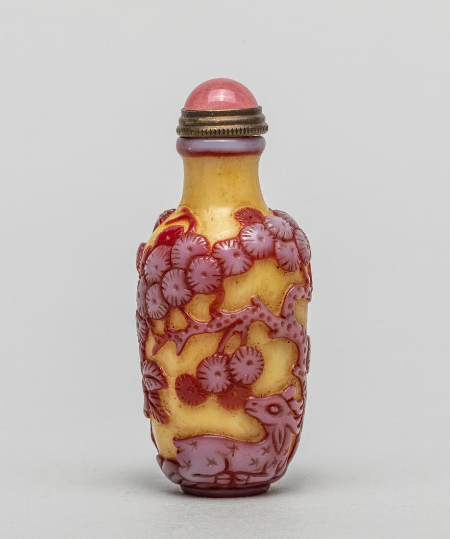 Chinese Overlay Glass Snuff Bottle: Of vase form, carved around the body in raised relief with a bird, a deer, peony, pine tree and a seal mark, reserved in red tone on a yellow grounds with gemstone stopper. 3.05inch H, 1.3inch W.