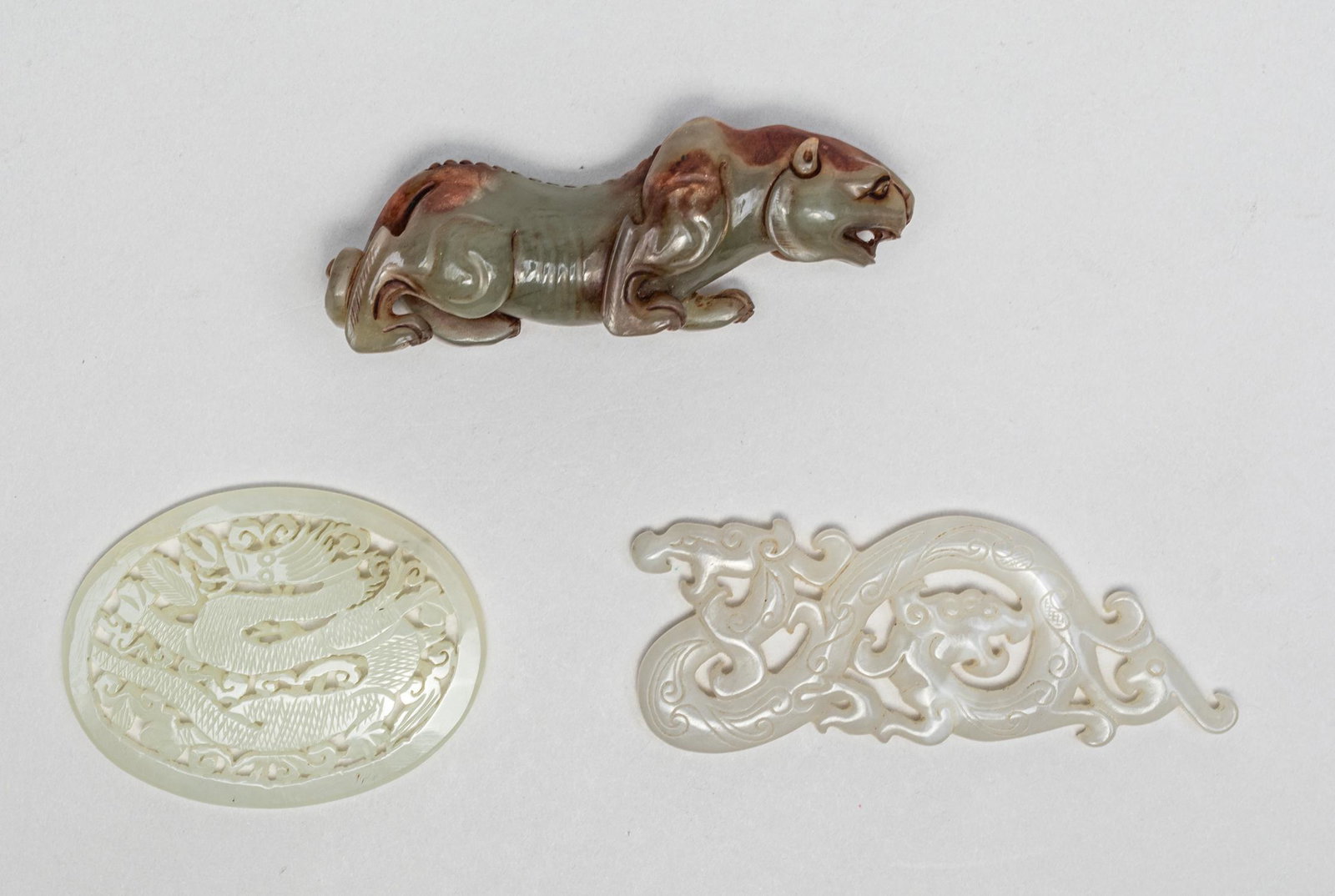Estate Chinese Jade/Hard Stone Carvings: Three as a group, one carved and pierced as a S-shaped sinuous dragon with twin heads, one of oval shape reticulated with a sinuous dragon among scrolling clouds, and a recumbent beast with building e