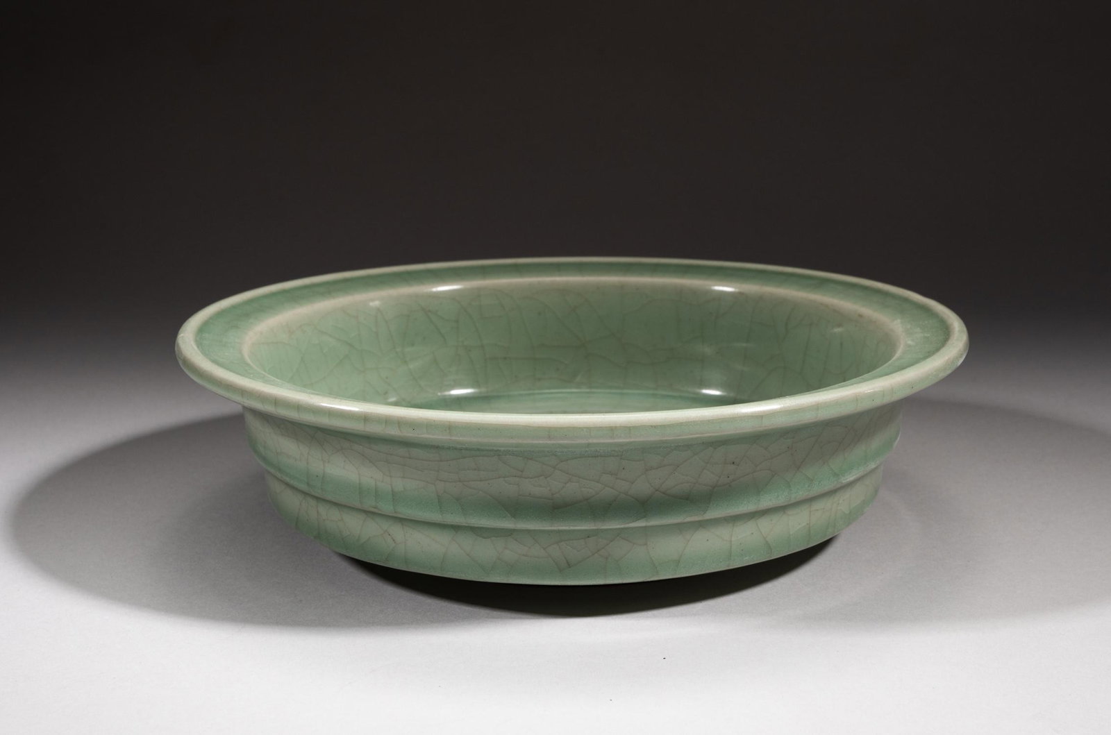 Chinese Ming Type Longquan Porcelain Brush Washer: The interior centre carved in low relief with leafy branches, covered to the inside and out with a celadon green glaze suffused with a network of natural crackles, the unglazed base revealing the redd