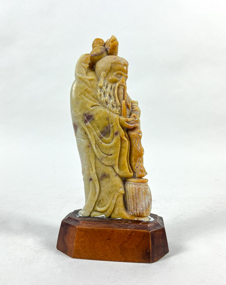 20 Century Chinese Shoushan Stone Sculpture: Carved as an old man with right hand holding a pipe and left hand holding a tall shaft with a dragon terminal suspending with double gourd and fish, with a fish basket along his feet, with a wood stan