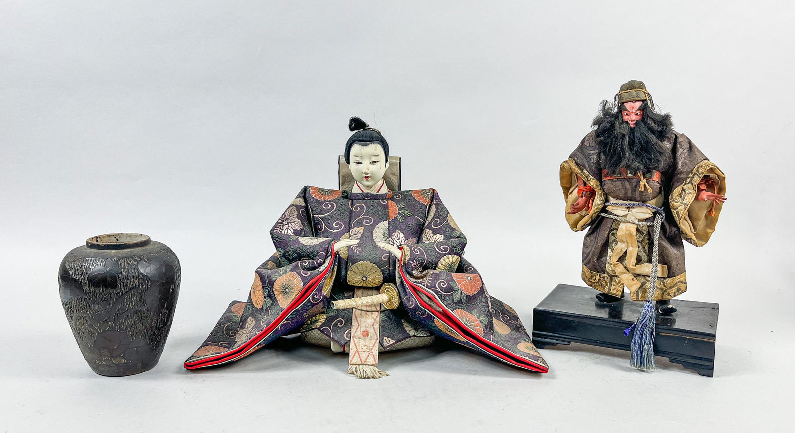 Old Japanese Doll & Porcelain Jar: Including two Japanese style dolls dressed in traditional costume and a black glazed porcelain jar carved in low relief with bird and flowers around the exterior. Approx. 13inch L, 7inch W, 8.5inch H