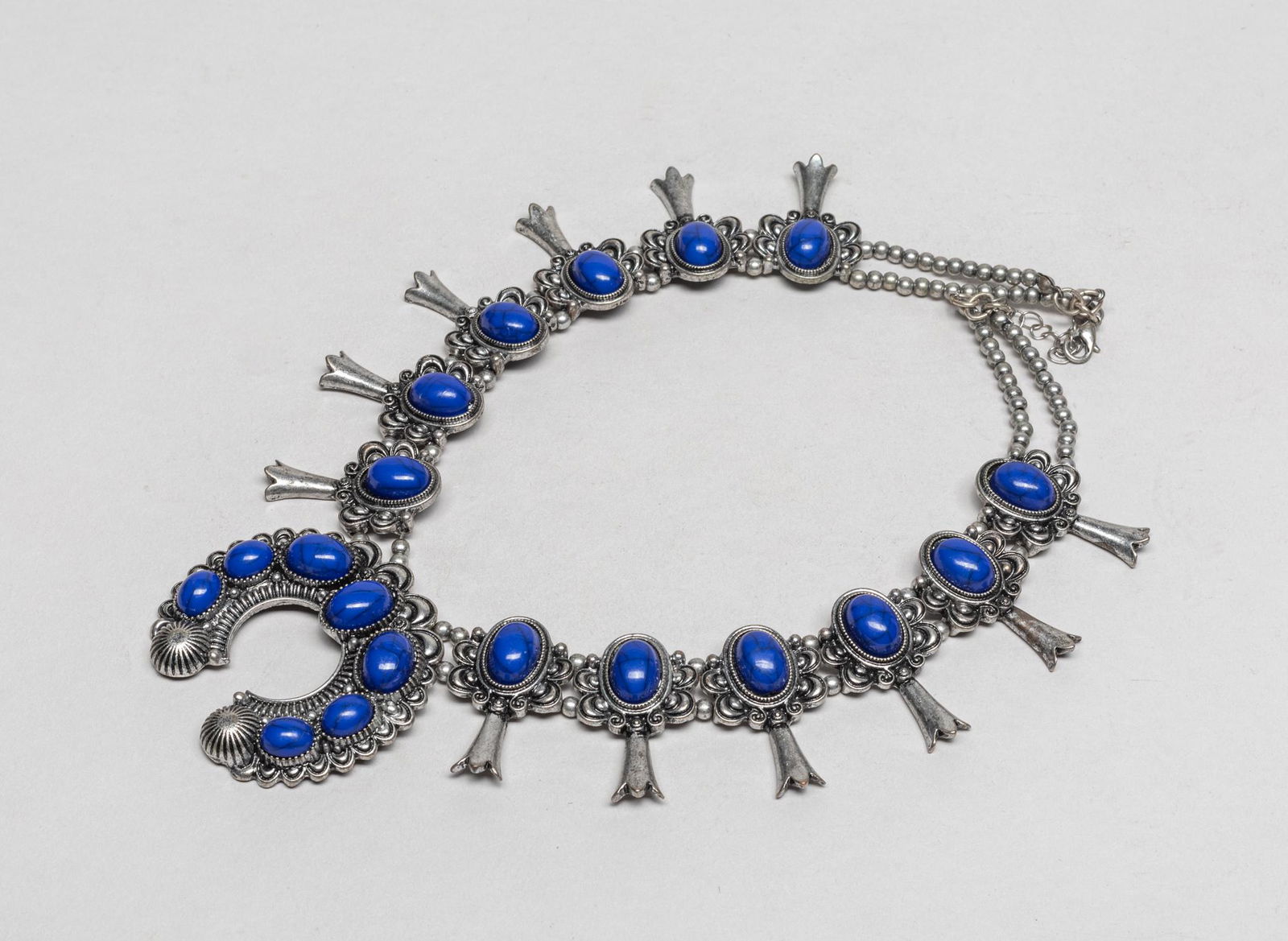 Designed Navajo Squash Blossom Necklace: Elaborate Navajo type silver-colored necklace, modeled in squash blossom form, decorated with lapis like stones. 16inch L.