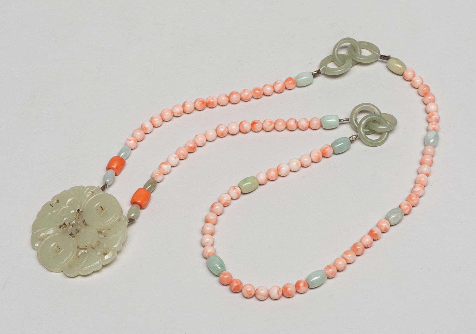 Chinese Jade & Coral Like Necklace: Collectible coral like bead necklace with interlocking celadon jade rings and a white jade plaque, carved in openwork with a bat, a peach branch and two coins, forming in circular shape. 28inch L.