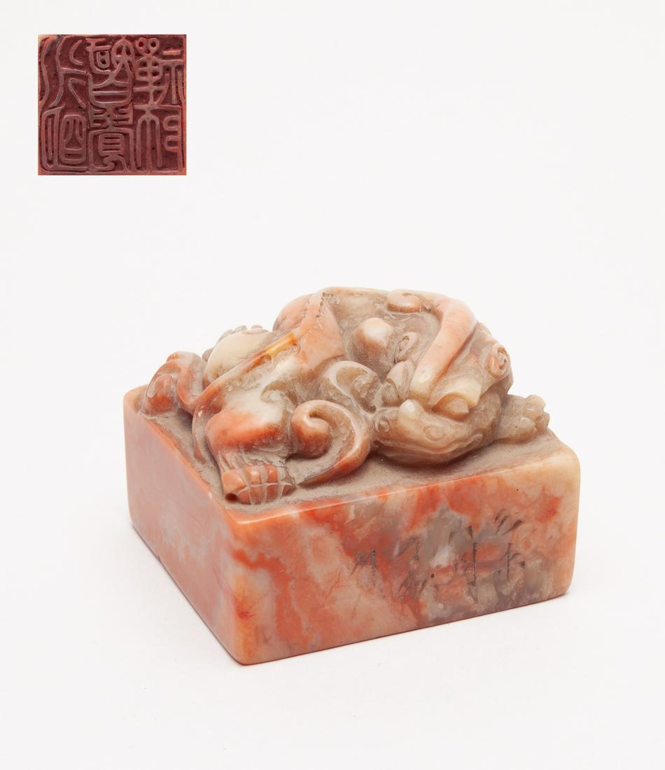 Large Chinese Shoushan Stone Seal: Of square section, with inscription on one side, surmounted by a crouching mythical beast with a muscular body and a bifurcated tail, the stone of a mixed red and brown-white tone. 2.6inch L, 2.45inch