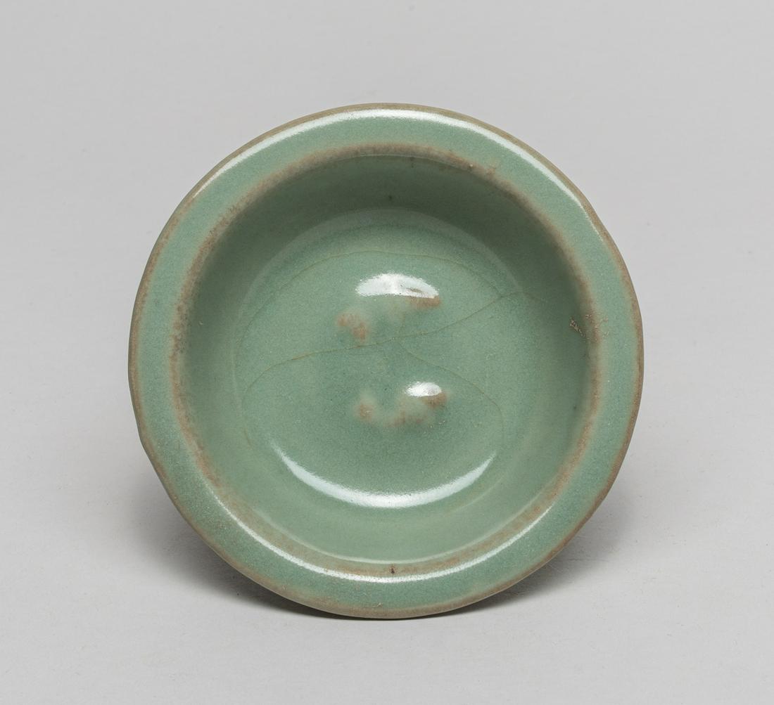 Korean Early Celadon Porcelain Cup: The rounded sides rising from a tapered foot to a flat rim, the interior centre moulded with a pair of swimming fish, the exterior with a band of lotus petal, covered the inside and out with a celadon