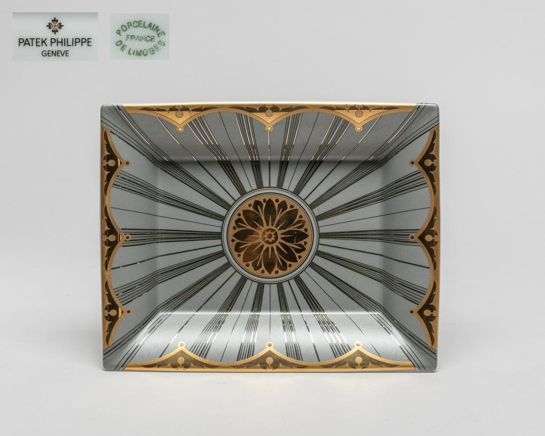 Patek Philippe Porcelain Sun Plate/Tray: Of rectangular form, the inside enameled with gray and silver colored lines radiating from a central golden-colored flower, the bottom marked Patek Philippe Geneve Porcelaine France De Limoges Collect