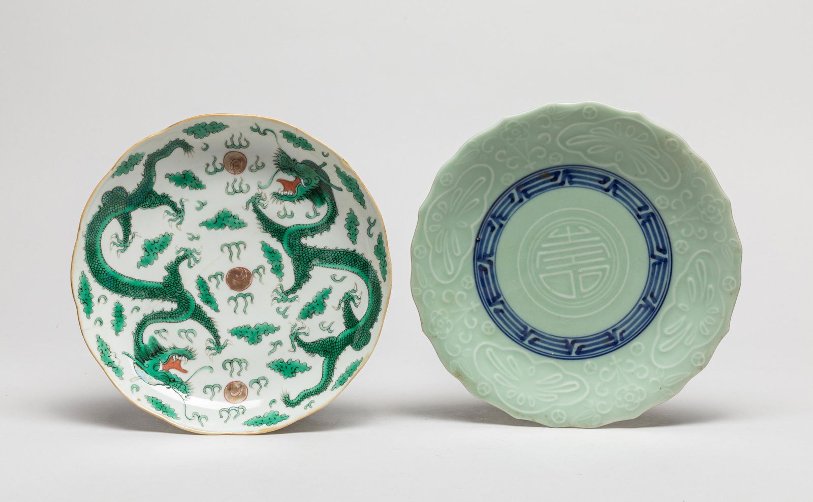 Two Chinese Export Porcelain Plates: One enameled in green with two dragons pursuing flaming pearls amidst clouds, the base with a seal mark, the other carved with stylized shou character and flowers on a celadon ground. 7.3inch W (large
