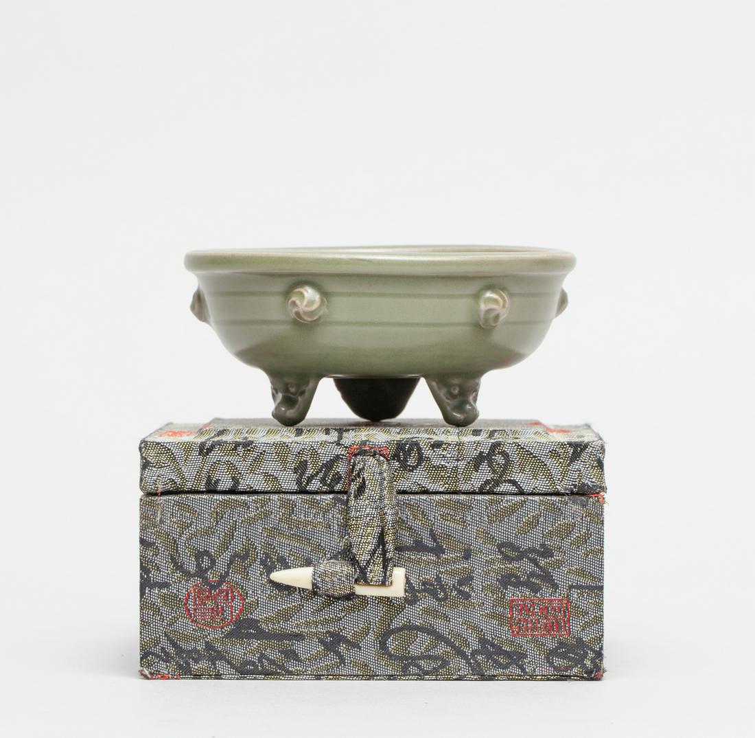 Chinese Yaochou Type Porcelain Washer: The compressed body supported on three short mask feet, the sides set with six raised bosses, the interior carved in low relief with a stylized flower, covered overall with an celadon green glaze save