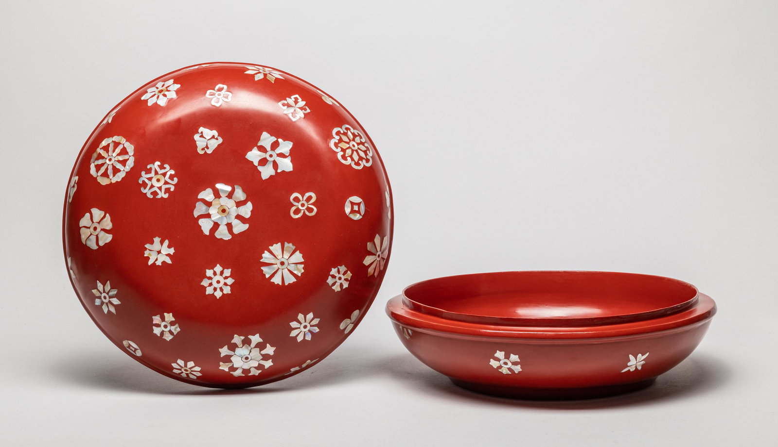 Large Korean Lacquer Box Inlaid MOP: Large red lacquer covered box of circular shape, the exterior inlaid with mother of pearl as flowers and coins on a red ground. 12.2inch W, 5.5inch H.